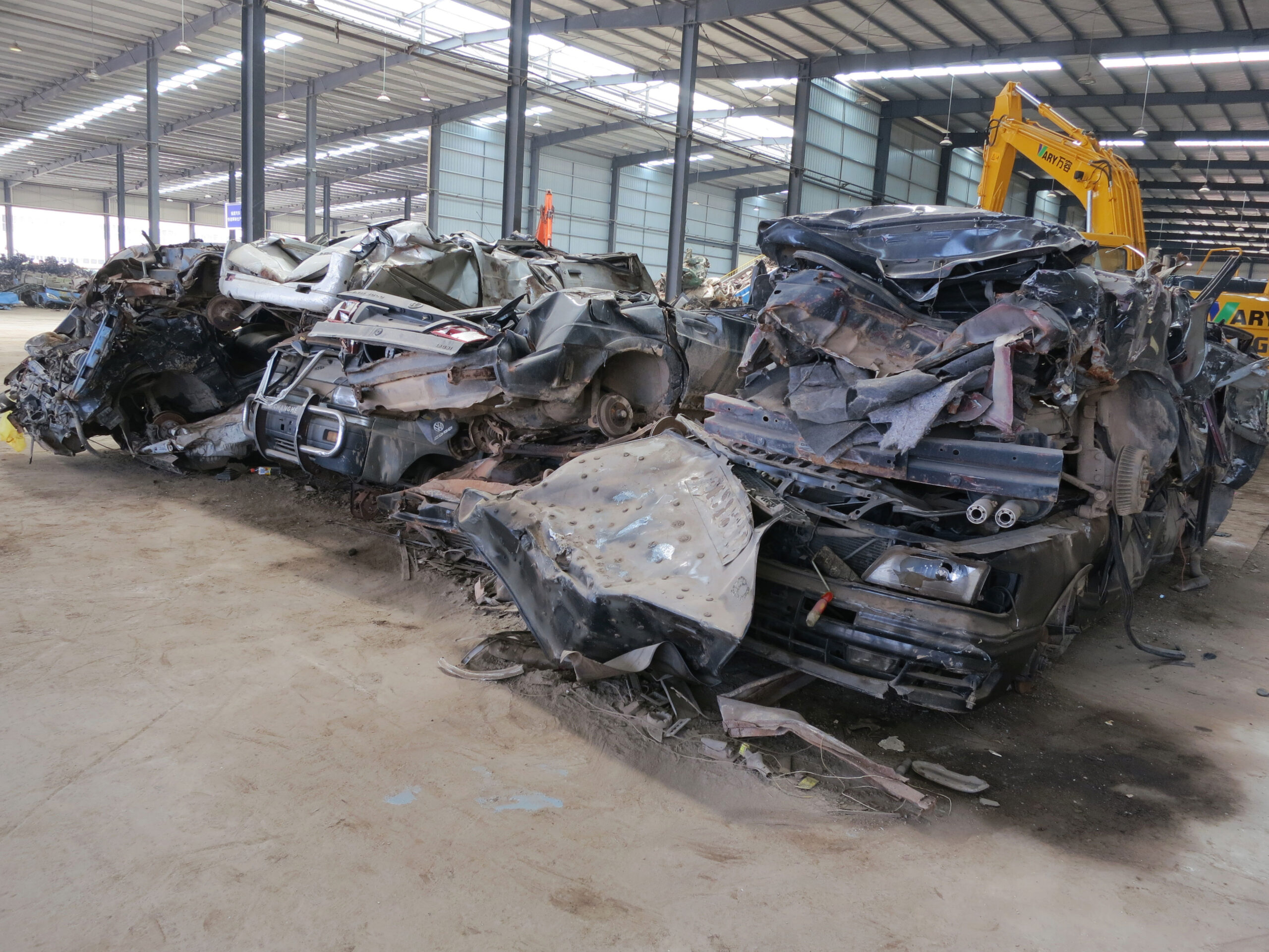 Three crushed automobiles with a yellow front loader in the background